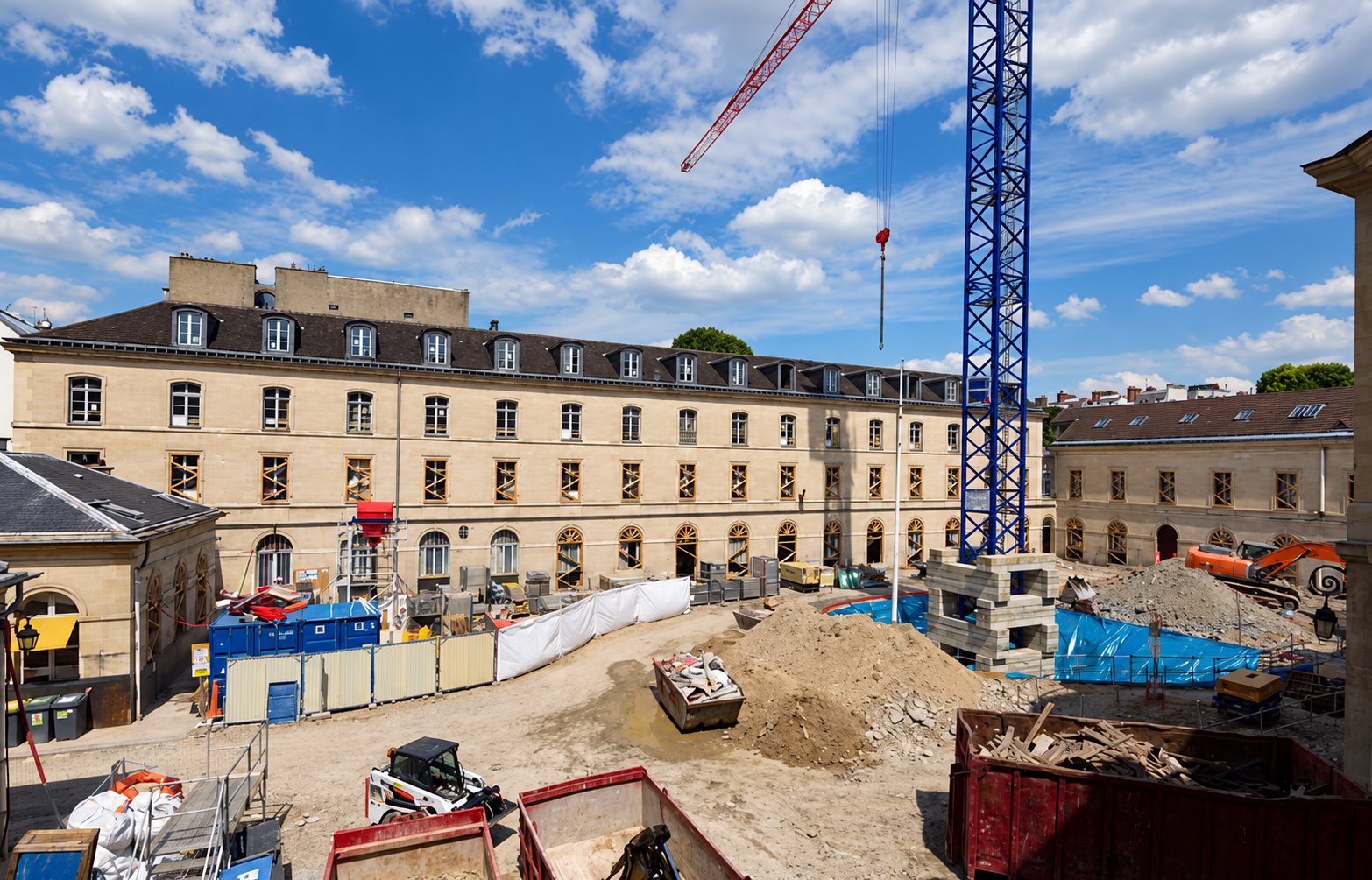 Un vaste chantier de rénovation devant un long bâtiment en pierre, avec une grue à tour, des engins de terrassement, des tas de terre et des bennes.