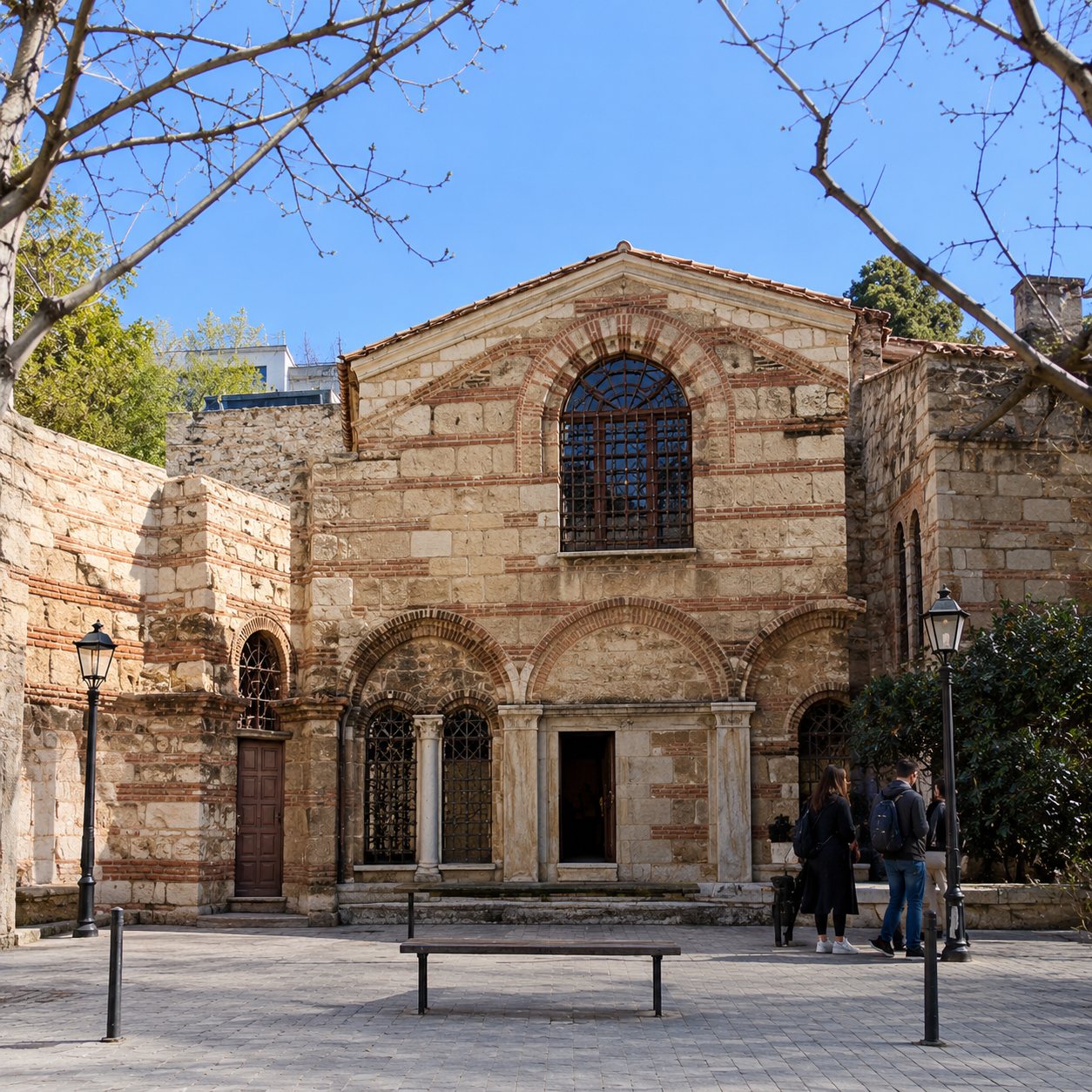 Façade d'un bâtiment ancien en pierre claire orné d'un grand arc et d'une rosace, entouré d'arbres presque nus sous un ciel bleu.