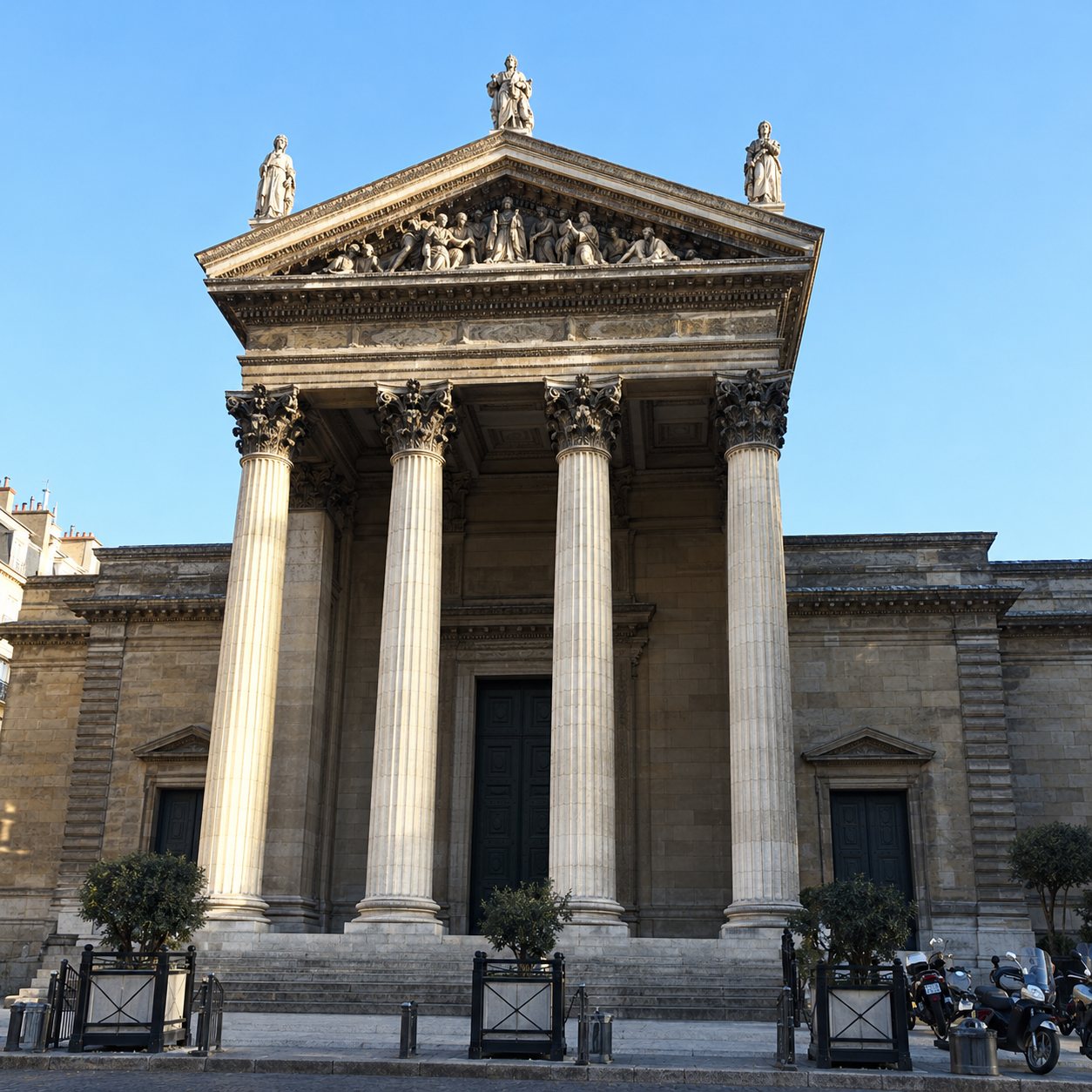 Façade d'un bâtiment néoclassique en pierre avec quatre colonnes et un fronton sculpté, sous un ciel bleu dégagé.