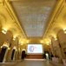 Vue d'une grande salle richement décorée aux murs éclairés, avec un plafond vitré et un écran lumineux au fond.